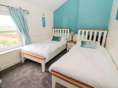 A bedroom with two single beds a window with blue curtains and a bedside table with a lamp at St Cuthberts Cottage in Beal near Holy Island
