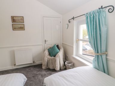A bedroom corner with a fluffy chair and blue cushion near a window with blue curtains at St Cuthberts Cottage in Beal near Holy Island