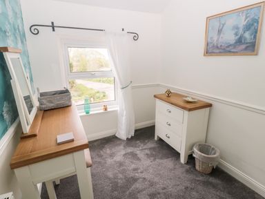 A room with a window curtain dresser mirror chest of drawers picture and waste basket at St Cuthberts Cottage in Beal near Holy Island