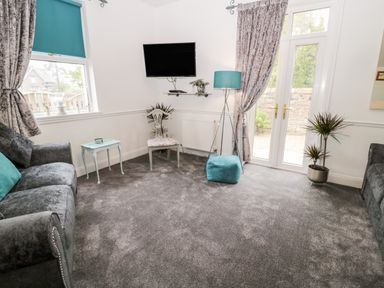 A sitting room with two sofas a TV chair floor lamp and French doors at St Cuthberts Cottage in Beal near Holy Island