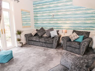 A living room with gray sofas cushions a lamp plant and glass doors at St Cuthberts Cottage in Beal near Holy Island
