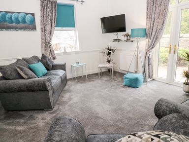 A living room with grey sofas a wall-mounted TV and a floor lamp at St Cuthberts Cottage in Beal near Holy Island