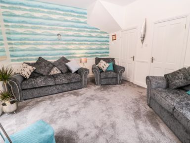 A living room with grey sofas and an armchair with cushions and a blue and white striped wallpaper at St Cuthberts Cottage Beal near Holy Island