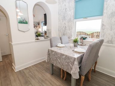 A dining area with four chairs around a table set for two people with a window and blue blind at St Cuthbert's Cottage Beal near Holy Island