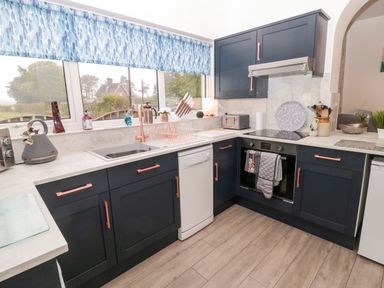A kitchen with dark cabinets white countertops and a window with blue patterned blinds at St Cuthberts Cottage in Beal near Holy Island