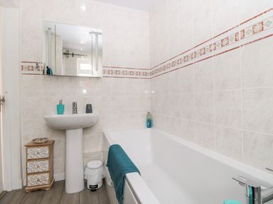 A bathroom with a bathtub a sink a mirror and a small cabinet at St Cuthberts Cottage Beal near Holy Island