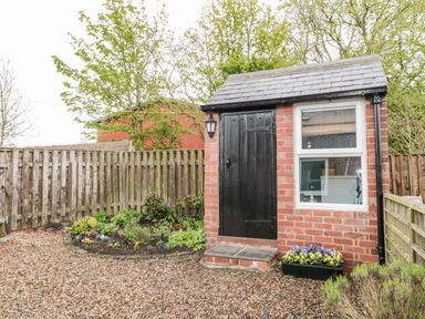 A small brick outbuilding with a black door and window surrounded by gravel and a wooden fence at St Cuthberts Cottage in Beal near Holy Island