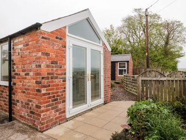 A small brick building with white double doors next to a wooden fence and garden at St Cuthberts Cottage Beal near Holy Island