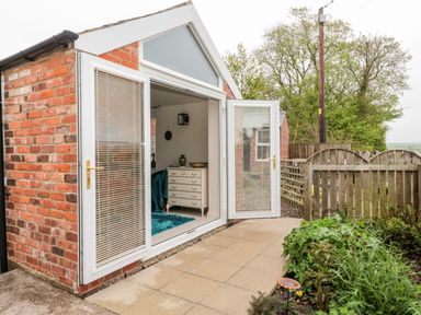 An open door leading from a brick building to a patio with plants and a wooden fence at St Cuthberts Cottage in Beal near Holy Island