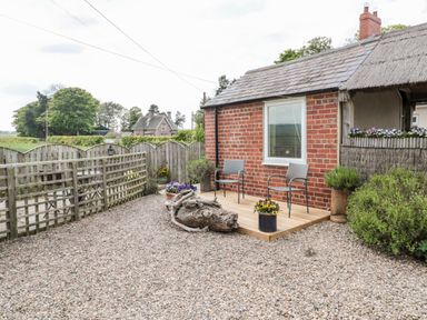 A small wooden patio with two chairs and flower pots outside a brick cottage at St Cuthberts Cottage in Beal near Holy Island