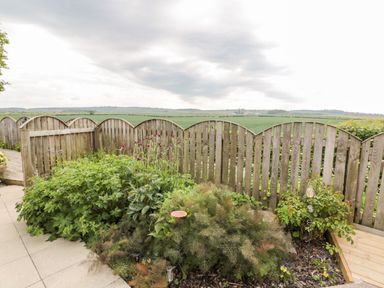 A garden with various plants and flowers next to a wooden fence overlooking fields at St Cuthbert's Cottage in Beal near Holy Island