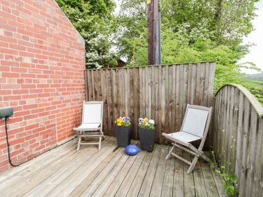 A wooden deck with two chairs and two flower pots against a brick wall and wooden fence at St Cuthberts Cottage in Beal near Holy Island