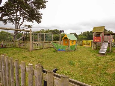 An outdoor playground with wooden fences a green boat play structure a slide and climbing frames at Rose Cottage in St Dogmaels near Cardigan