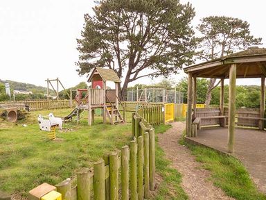 An outdoor playground with wooden climbing structure slide spring rider and a wooden gazebo in a grassy area at Rose Cottage St Dogmaels near Cardigan