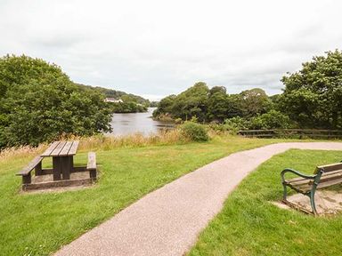 A park with a wooden picnic table bench and a metal bench near a river at Rose Cottage in St Dogmaels near Cardigan