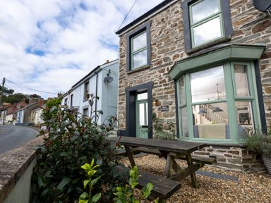 Exterior view of a stone cottage with green windows and door and a wooden picnic table in front at Rose Cottage in St Dogmaels near Cardigan