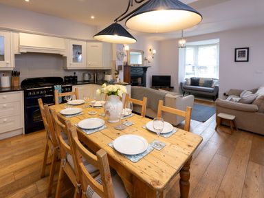 An open plan kitchen and living room with a wooden dining table set with plates and glasses Rose Cottage in St Dogmaels near Cardigan
