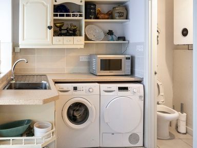 A laundry room with a sink washing machine dryer microwave and various items on shelves at Rose Cottage in St Dogmaels near Cardigan