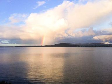 A large body of water with a distant shoreline and a rainbow under a cloudy sky at The Beach House Apartment in Buncrana County Donegal