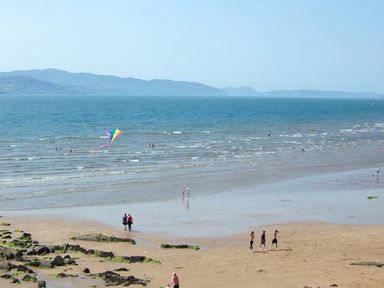 A beach with people walking and playing near the water and a kite flying at The Beach House Apartment in Buncrana County Donegal
