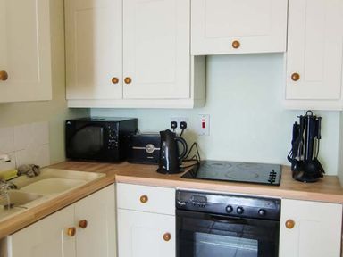 A kitchen with white cabinets wooden knobs a microwave toaster kettle utensils and an oven at The Beach House Apartment in Buncrana County Donegal