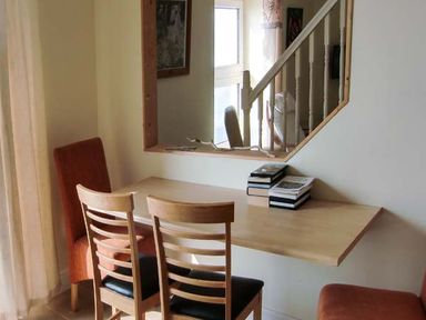 A dining area with a wooden table attached to the wall two wooden chairs and two red upholstered chairs near a window with a mirror above the table at The Beach House Apartment in Buncrana County Donegal