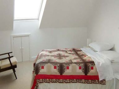 A bedroom with a bed covered with a patchwork quilt a wooden chair and a skylight window at The Beach House Apartment in Buncrana County Donegal
