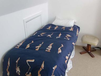 A single bed with a pillow and a blue patterned duvet beside a small padded stool at The Beach House Apartment in Buncrana County Donegal