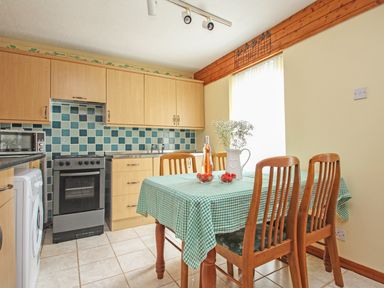 A kitchen with wooden cabinets and a tiled backsplash with a table covered by a green checkered tablecloth and wooden chairs at 4 Manorcombe  Honicombe Manor near Gunnislake