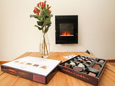 A wooden table with a box of chocolates and a glass vase with red berries in front of a wall-mounted fireplace at 4 Manorcombe  Honicombe Manor near Gunnislake