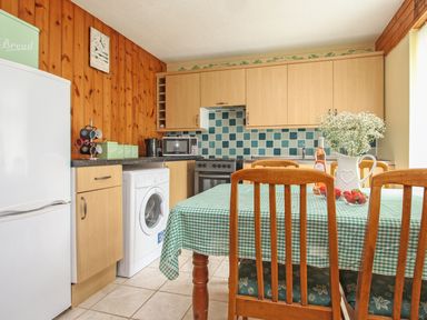 A kitchen with wooden cabinets a washing machine a table with a green checkered tablecloth and chairs at 4 Manorcombe Honicombe Manor near Gunnislake