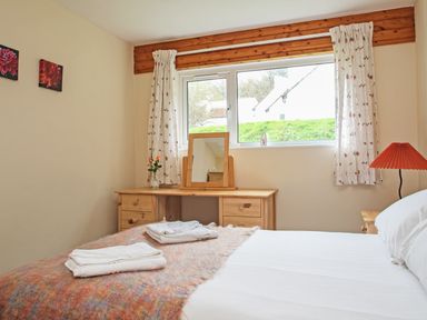 A bedroom with a bed side table a lamp a dressing table with a mirror and a window with floral curtains at 4 Manorcombe  Honicombe Manor near Gunnislake