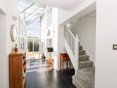 A hallway with staircase carpeted stairs and wooden furniture next to glass wall and door at 1 Atlantic Haven in Llangennith
