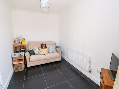 A small room with a beige sofa with cushions a wooden shelf with toys a radiator and a small television on a wooden stand at 1 Atlantic Haven in Llangennith