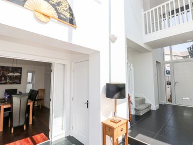 A hallway with black tiled floor wooden side table with lamp staircase and entrance door at 1 Atlantic Haven in Llangennith