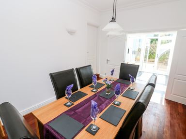 A dining room with a wooden table set for six with black leather chairs and purple napkins at 1 Atlantic Haven in Llangennith