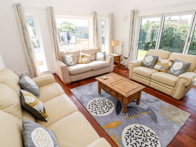A living room with two cream sofas one beige sofa wooden coffee table and large windows at 1 Atlantic Haven in Llangennith