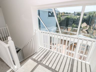 A staircase with white railings and a large slanted window overlooking a garden at 1 Atlantic Haven in Llangennith