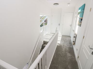 A carpeted hallway with white doors a staircase with a white railing and a painting on the wall at 1 Atlantic Haven in Llangennith