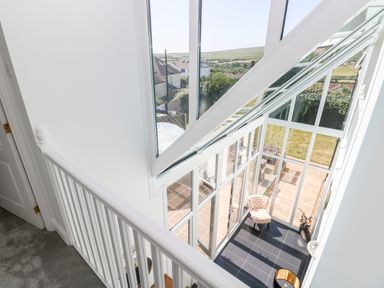 A white railing overlooking a sunroom with glass walls and a chair at 1 Atlantic Haven in Llangennith