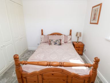 A bedroom with a wooden bed and matching bedside table with a lamp at 1 Atlantic Haven in Llangennith
