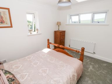 A bedroom with a wooden bed a wooden chest of drawers a table lamp and three windows at 1 Atlantic Haven in Llangennith