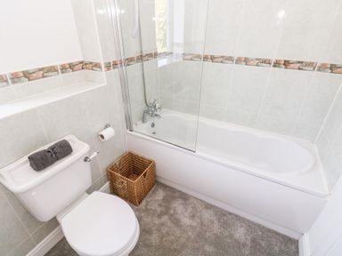 A bathroom with a toilet a bathtub with a glass shower screen and a woven basket on the floor at 1 Atlantic Haven in Llangennith