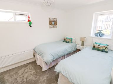 A bedroom with two single beds a bedside table with a lamp and two windows at 1 Atlantic Haven in Llangennith
