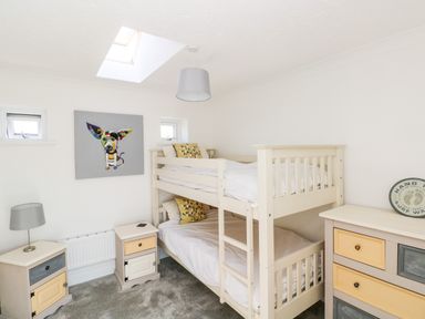 A bedroom with a bunk bed nightstands a chest of drawers and a painting of a dog at 1 Atlantic Haven in Llangennith