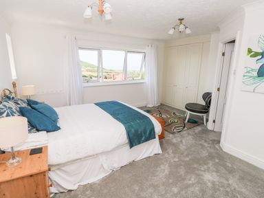 A bedroom with a bed blue pillows and runner wooden bedside tables a large window wardrobe a chair and a rug at 1 Atlantic Haven in Llangennith