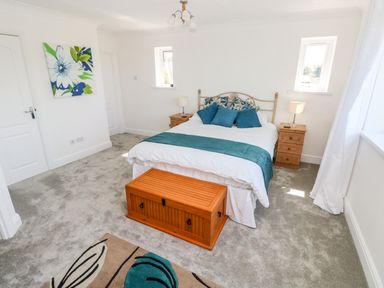 A bedroom with a bed bedside tables lamps a wooden chest a floral painting and carpet at 1 Atlantic Haven in Llangennith