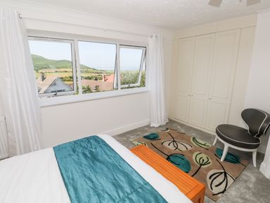 A bedroom with a bed a patterned rug a chair built in wardrobes and a window with a view at 1 Atlantic Haven in Llangennith