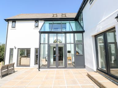 An exterior view of a modern white house with large glass doors and windows and a tiled patio at 1 Atlantic Haven in Llangennith