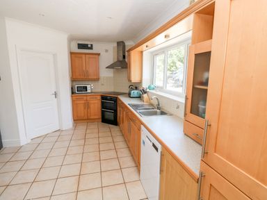 A kitchen with wooden cabinets a double sink a dishwasher an oven a microwave and tiled flooring at 1 Atlantic Haven in Llangennith